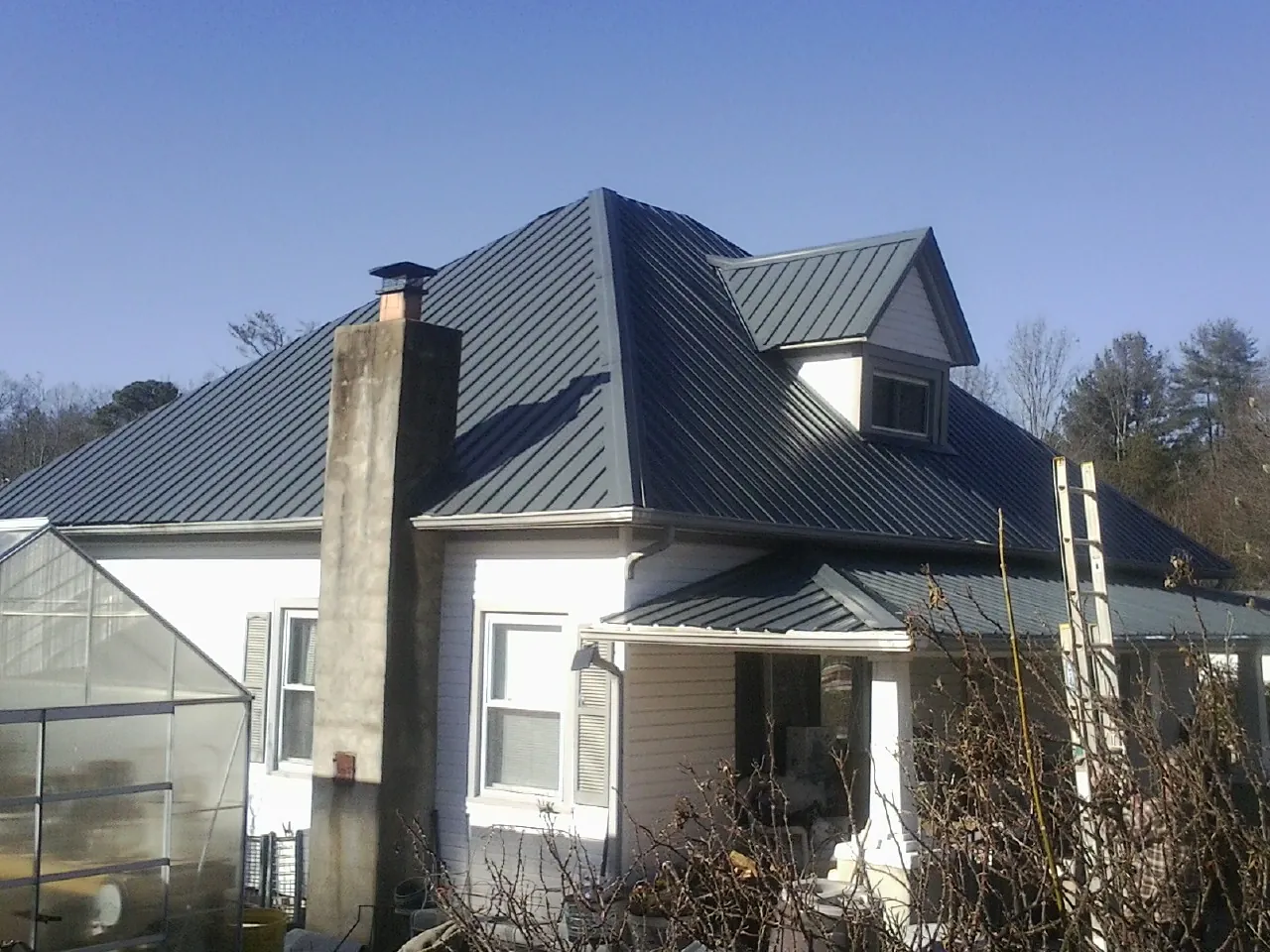 Dark blue standing seam metal roof on a white farmhouse with dormer — Slate & Tile Roof Repair by Roofing Brothers in Buck Creek