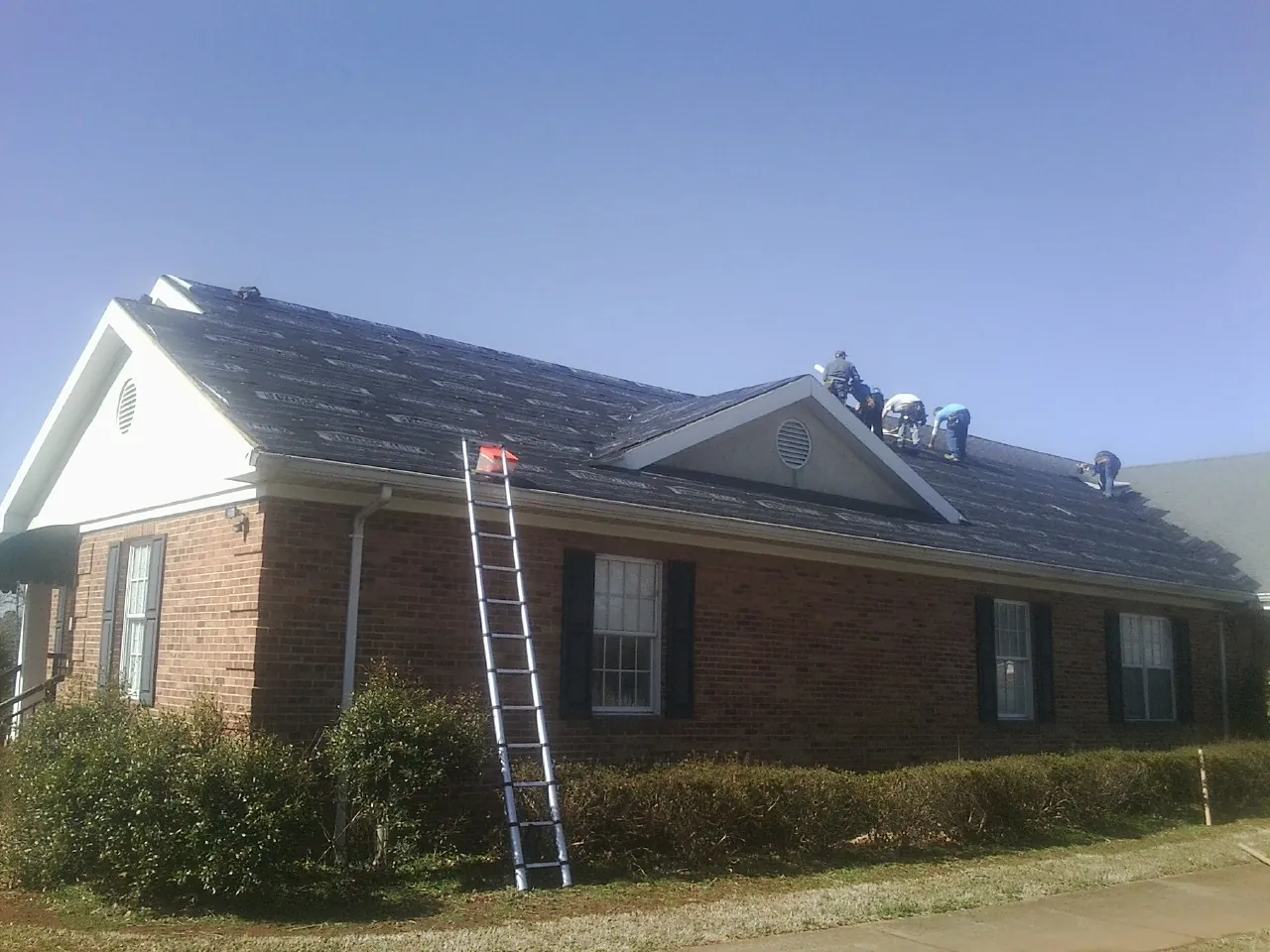Crew tearing shingles off a brick ranch roof with a ladder set — Emergency Roof Repair work by our crew in Buck Creek