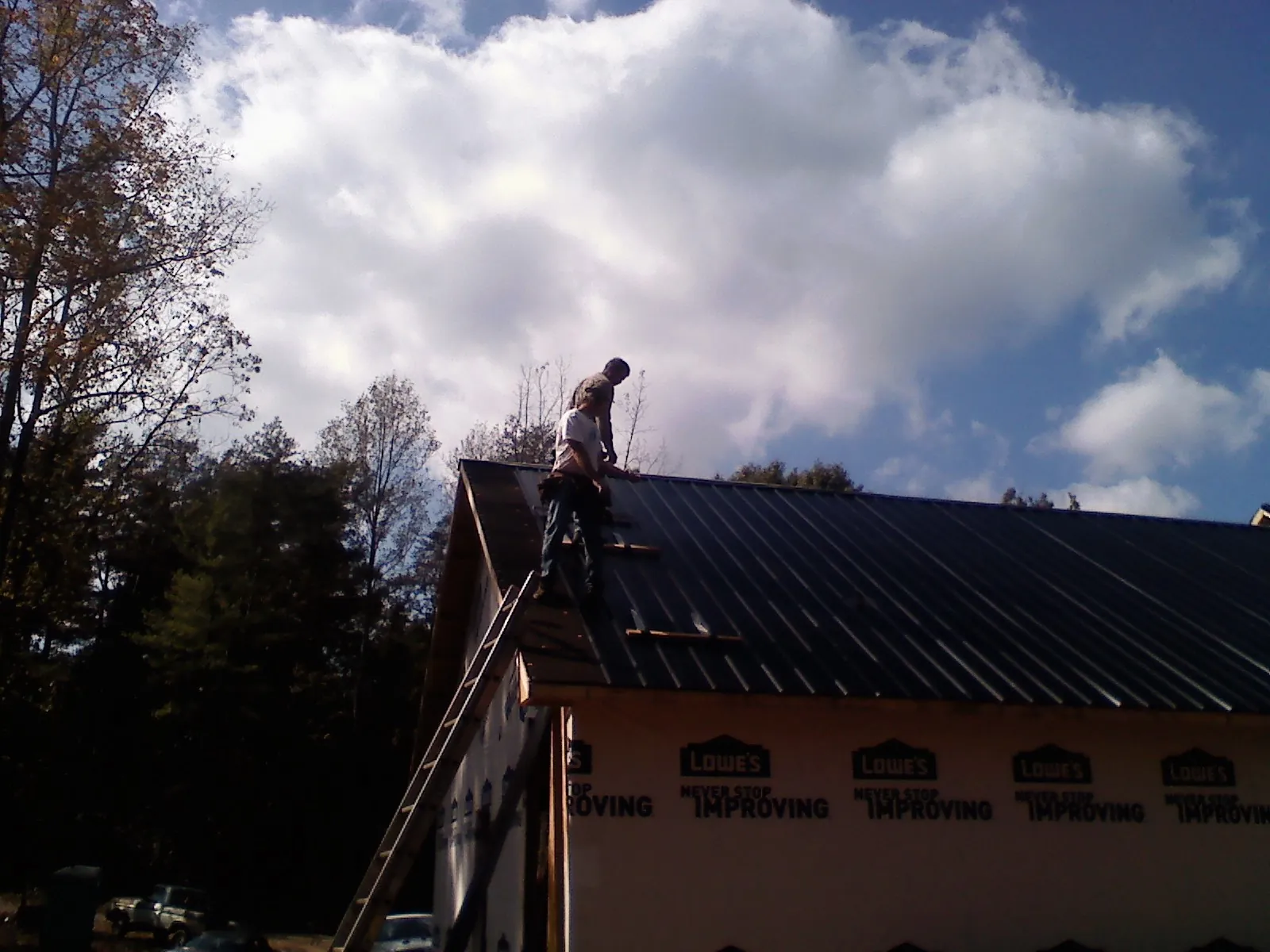 Roofer fastening dark metal panels high against a cloudy sky, from a Roof Inspection job in Buck Creek