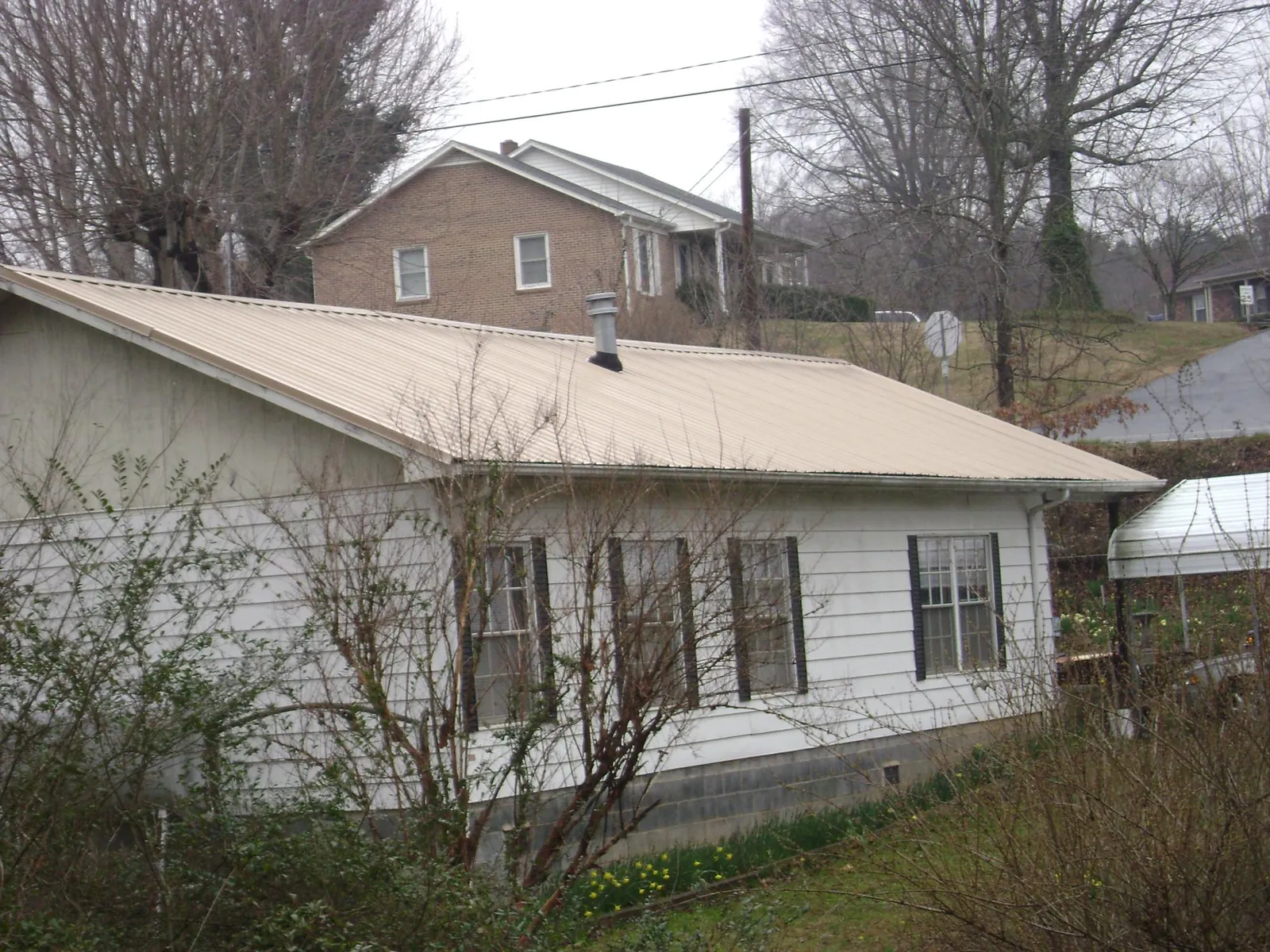 Tan metal roof on a white sided house set into a hillside — Commercial Roofing by Roofing Brothers in Buck Creek